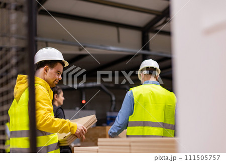 Young man with Down syndrome working in modern factory, colleague teaching him about his job, showing process. Concept of workers with disabilities, support in workplace. 111505757