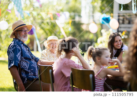 Family chatting, and having fun at party table during summer garden party. Grandfather sitting at head of table. 111505795