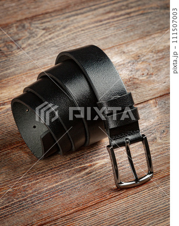 Black leather belt on a wooden brown background. 111507003