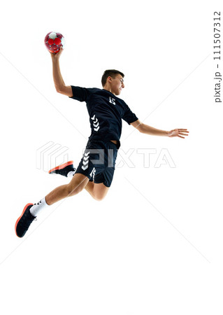 Full-length image of young handball athlete in motion during game, throwing ball against white studio background. Motivation to win 111507312