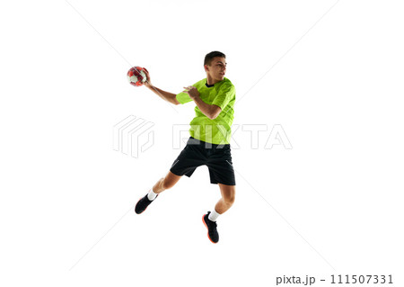 Competitive young guy in uniform, handball player in a jump, throwing ball during game against white studio background 111507331