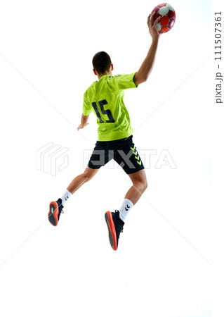 Dynamic back view image of young guy in uniform handball playing in motion, jumping with ball against white studio background Dynamic back view image of young guy in uniform handball playing in motion, jumping with ball against white studio background 111507361