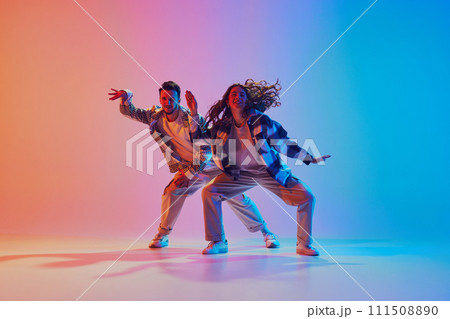 portrait of attractive and fashion dressed par of dancers performing harmony in motion against gradient studio background. portrait of attractive and fashion dressed par of dancers performing harmony in motion against gradient studio background. 111508890