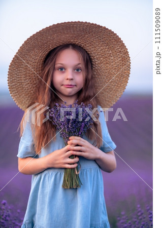 Girl lavender field in a blue dress with flowing hair in a hat stands in a lilac lavender field 111509089
