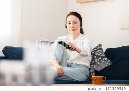 部屋のソファーでテレビを見ながらくつろぐ女性 111509519