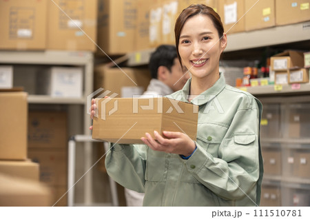 笑顔で段ボールを持つ作業服を着た女性 111510781