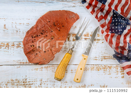 Preparation raw beef steak on table in honor American holidays is accompanied by display of USA flag Preparation raw beef steak on table in honor American holidays is accompanied by display of USA flag 111510992