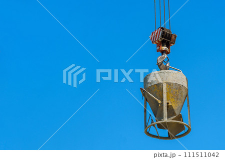 Tower crane lifting a concrete bucket for pour of concrete cement mix into formwork at construction process 111511042