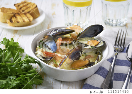 Creamy soup with mussels and shrimps served with lemon and parsley on a white table. Creamy soup with mussels and shrimps served with lemon and parsley on a white table. 111514416