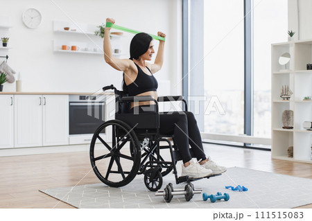 Caucasian woman in wheelchair stretching bands while exercising. 111515083