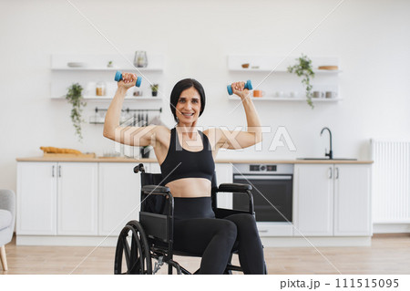 Caucasian person with disability holding dumbbells in raised arms. 111515095
