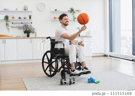 Bearded adult with mobility impairment dribbling ball in studio apartment. 111515109