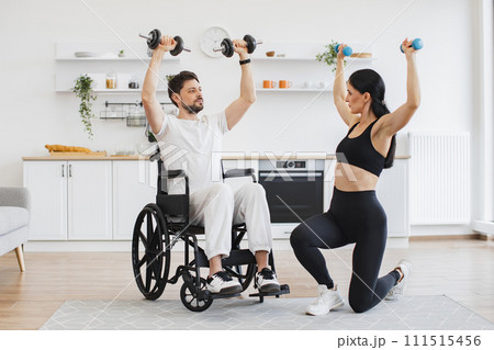 Physiotherapist helping adult man in wheelchair to workout with dumbbells. Physiotherapist helping adult man in wheelchair to workout with dumbbells. 111515456
