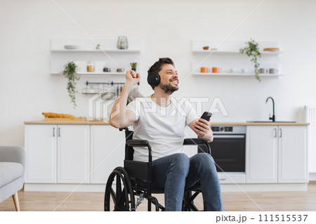 Man in wheelchair and headphones moving hands in air at kitchen. Man in wheelchair and headphones moving hands in air at kitchen. 111515537