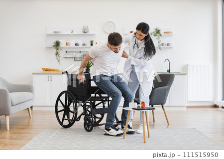 Man standing near wheelchair while physician giving him hand at home. Man standing near wheelchair while physician giving him hand at home. 111515950