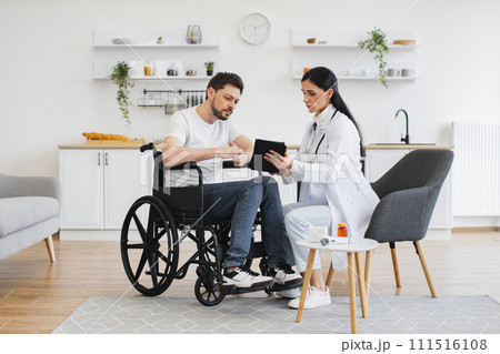 Female brunette doctor checking up condition of bearded male patient at home. 111516108