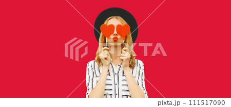 Portrait of beautiful young woman blowing her lips sends kiss with sweet red heart shaped lollipop Portrait of beautiful young woman blowing her lips sends kiss with sweet red heart shaped lollipop 111517090