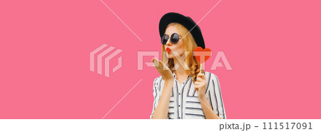 Portrait of beautiful young woman blowing her lips sends kiss with sweet red heart shaped lollipop 111517091