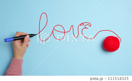 A woman's hand wrote love with a red felt-tip pen and a ball of wool 111518325