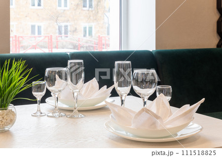 Glasses, plates, napkins served for dinner in restaurant with cozy interior. 111518825