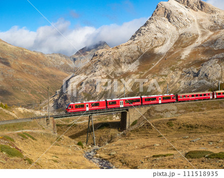 Bernina, Switzerland - October 15th 2023: Red train of Rhaetian railway passing a bridge in alpine terrain. 111518935