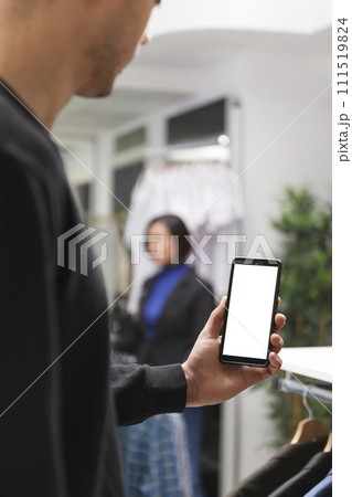 Clothing store customer holding smartphone with blank screen mockup while exploring apparel online. Boutique man hand using mobile phone with empty white display while shopping in mall Clothing store customer holding smartphone with blank screen mockup while exploring apparel online. Boutique man hand using mobile phone with empty white display while shopping in mall 111519824
