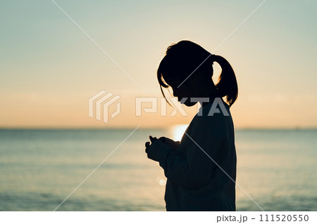 夕焼けの中、海辺に立つ女の子。 111520550
