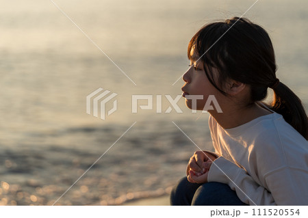 夕焼けの中、海辺に立つ女の子。 111520554