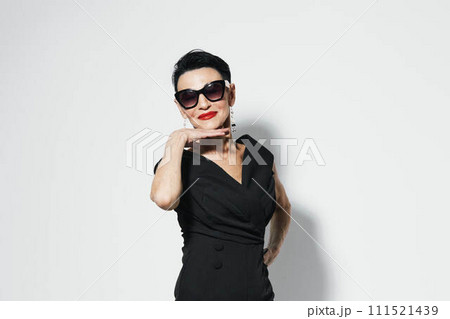 Stylish woman in black dress and sunglasses posing confidently for the camera with hand on hip 111521439