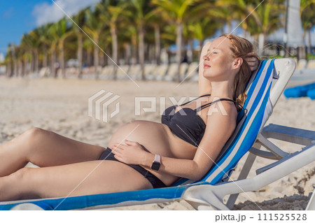 Basking in seaside tranquility, a pregnant woman lounges on a sun lounger, embracing the soothing ambiance of the beach for a moment of serene relaxation Basking in seaside tranquility, a pregnant woman lounges on a sun lounger, embracing the soothing ambiance of the beach for a moment of serene relaxation 111525528