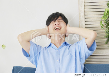 リビングで耳を塞ぐ男性 111526073