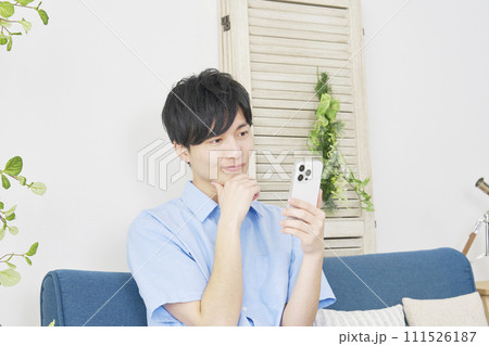リビングで考えながらスマートフォンを使う男性 111526187