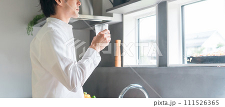 キッチンで水・白湯を飲む白シャツ姿の男性 111526365