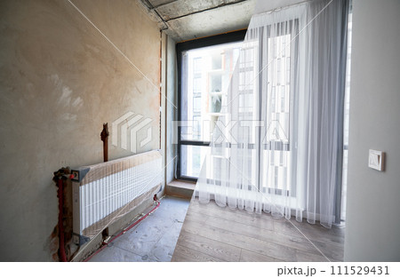Comparison of apartment flat before and after restoration or refurbishment. Photo collage of old room with large windows and new renovated room with heating radiator, parquet floor and white walls. 111529431