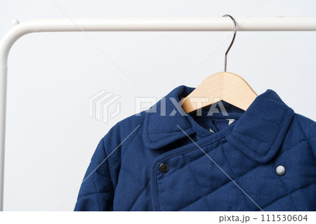 Blue quilted kids coat on hanger against white wall Blue quilted kids coat on hanger against white wall 111530604