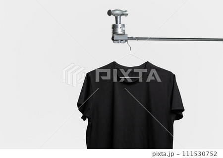 Plain black T-shirt hanging on hanger on gray background Plain black T-shirt hanging on hanger on gray background 111530752