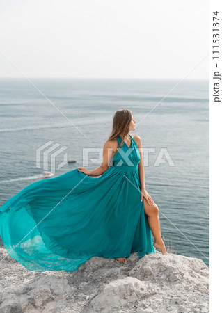 Woman sea trevel green dress. Side view a happy woman with long hair in a long mint dress posing on a beach with calm sea bokeh lights on sunny day. Girl on the nature on blue sky background. 111531374