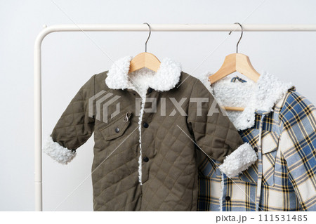 Two kids winter coats hanging on hangers against white wall 111531485