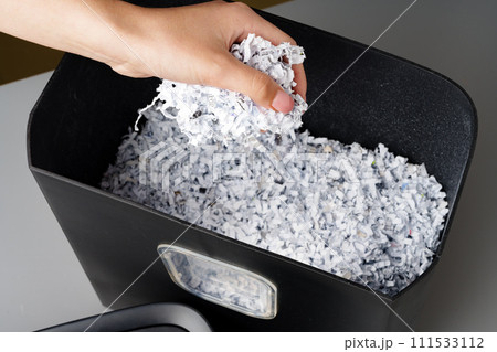 Hand using paper shredding machine against gray background Hand using paper shredding machine against gray background 111533112