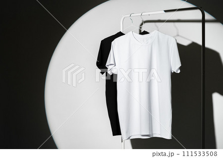 Black and white T-shirts hanging against white background studio shot Black and white T-shirts hanging against white background studio shot 111533508