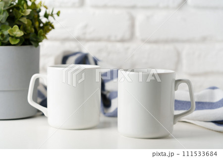 Two mugs on white table against brick wall background 111533684