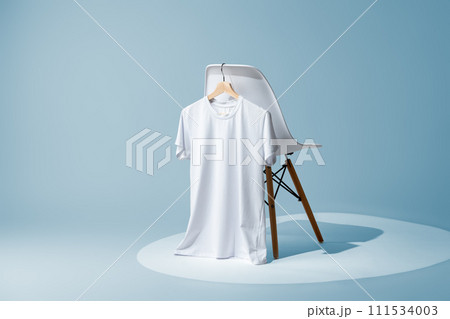 White blank t-shirt hanging on chair against blue wall White blank t-shirt hanging on chair against blue wall 111534003