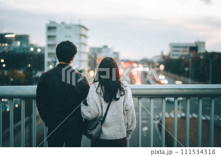 夕暮れ時に歩道橋から街中を眺めるカップル 夕暮れ時に歩道橋から街中を眺めるカップル 111534318