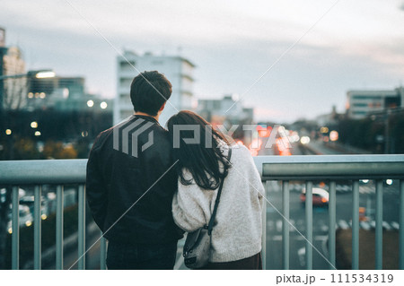 肩にもたれかかり、夕暮れ時に歩道橋から街中を眺めるカップル 111534319
