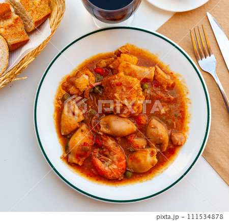 Catalan cuisine zarzuela with shrimp served on white plate on wooden table 111534878
