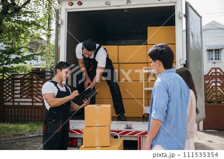 Professional movers assist a satisfied newlywed couple who sign the delivery checklist after furniture upload. Teamwork ensures a happy customer relocation. Moving Day Concept Professional movers assist a satisfied newlywed couple who sign the delivery checklist after furniture upload. Teamwork ensures a happy customer relocation. Moving Day Concept 111535354