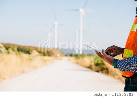 Engineer hold tablet in hand manages windmill farm. Generating clean energy the Asian technician's expertise ensures turbine efficiency. Global innovation and confidence in electricity control. Engineer hold tablet in hand manages windmill farm. Generating clean energy the Asian technician's expertise ensures turbine efficiency. Global innovation and confidence in electricity control. 111535382
