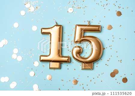 Gold candles in the form of number fifteen on blue background with confetti. 15 years celebration. 111535620