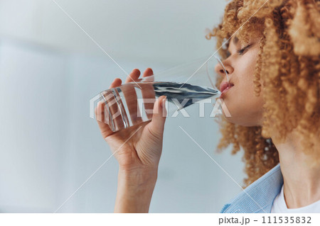 Woman with curly hair enjoying a refreshing drink of water from a glass in a healthy lifestyle concept 111535832
