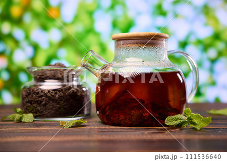 natural organic herbal tea in glass teapot and jar with dry tea on a wooden table natural organic herbal tea in glass teapot and jar with dry tea on a wooden table 111536640